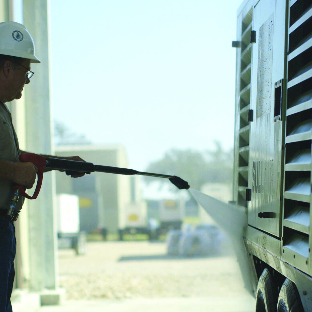 Worker in a hard hat pressure washing a piece of industrial equipment on a job site